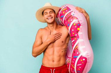 Mavi arka planda izole edilmiş şişme bir çörek tutan genç beyaz adam kahkahalar atıyor..