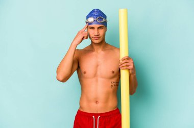 Kafkasyalı genç yüzücü elinde köpük sopa ile mavi arka planda izole edilmiş, parmağıyla şakağı işaret ederek bir göreve odaklanmış..