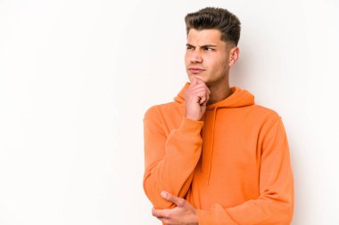 Beyaz arka planda izole edilmiş genç beyaz bir adam şüpheli ve şüpheci bir ifadeyle yana bakıyor..