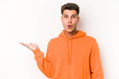 Beyaz arka planda izole edilmiş genç beyaz adam, avuç içi fotokopi alanını elinde tutmaktan etkilenmiş..