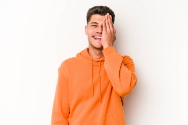 Beyaz arka planda izole edilmiş genç beyaz bir adam yüzünün yarısını palmiye ile örterek eğleniyor..