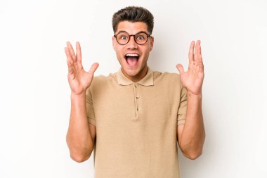 Beyaz arka planda izole olmuş genç beyaz bir adam zaferi veya başarıyı kutluyor, şaşırıyor ve şok oluyor..