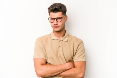 Beyaz arka planda izole edilmiş genç beyaz adam alaycı bir ifadeyle kameraya bakıyor..