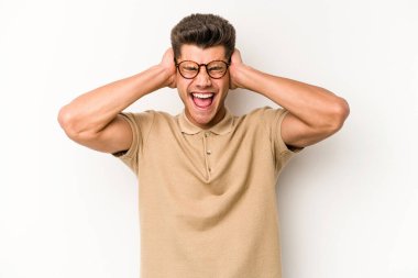 Beyaz arka planda izole edilmiş genç beyaz bir adam kulakları kulaklarıyla kapatıyor ve çok ses duymamaya çalışıyor..