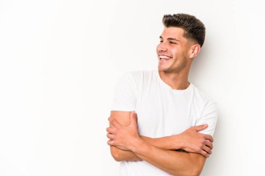 Beyaz arka planda izole edilmiş genç beyaz adam kollarını kavuşturarak gülümsüyor..
