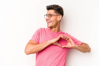 Beyaz arka planda izole edilmiş genç beyaz bir adam gülümsüyor ve elleriyle kalp şekli gösteriyor..