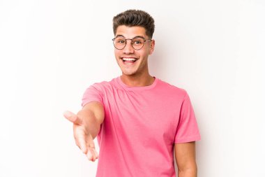 Beyaz arka planda izole edilmiş genç beyaz bir adam selamlama jesti olarak kameraya elini uzatıyor..