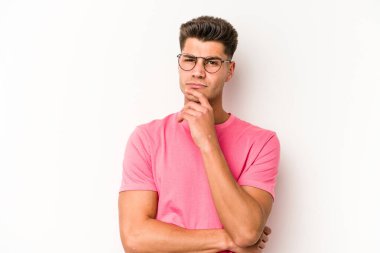 Beyaz arka planda izole edilmiş genç beyaz bir adam şüpheli, belirsiz, seni muayene ediyor..