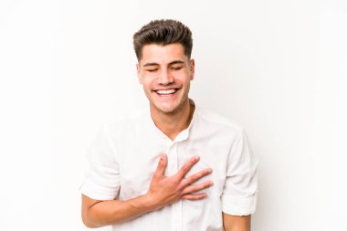 Beyaz arka planda izole genç beyaz adam yüksek sesle gülüyor elini göğsüne koyuyor..