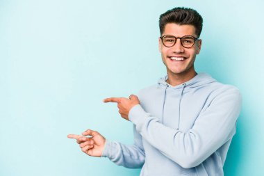 Kafkasyalı genç adam mavi arka planda izole edilmiş. İşaret parmağıyla işaret ettiği için heyecanlı..