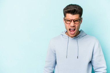 Kafkasyalı genç adam mavi arka planda izole edilmiş. Çok kızgın, öfkeli, hayal kırıklığına uğramış..