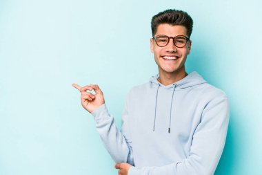 Mavi arka planda izole edilmiş genç beyaz adam işaret parmağıyla işaret ederek gülümsüyor..