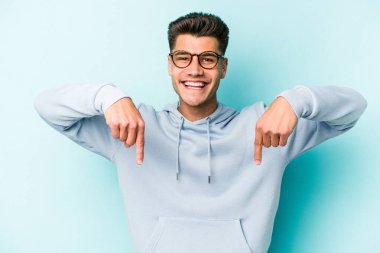 Kafkasyalı genç adam mavi arka planda izole edildi. Parmakları aşağıda, olumlu bir his var..