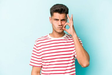 Genç beyaz adam mavi arka planda izole edilmiş ve parmakları dudaklarında bir sır saklıyor..