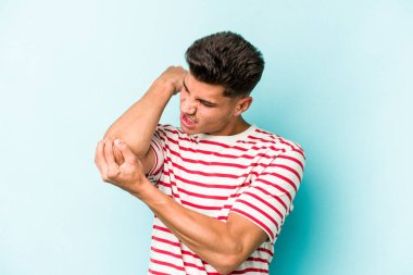 Kafkasyalı genç adam mavi arka planda izole edilmiş dirsek masajı yapıyor, kötü bir hareketin ardından acı çekiyor..