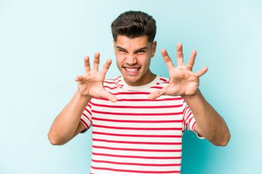 Mavi arka planda izole edilmiş genç beyaz adam pençelerini kedi taklidi yaparken gösteriyor, agresif bir hareket..