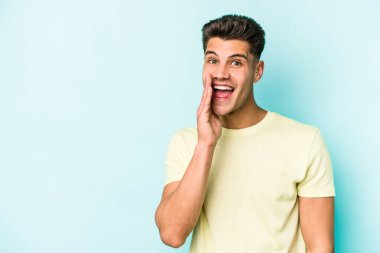 Mavi arka planda izole edilmiş genç beyaz adam yüksek sesle bağırıyor, gözleri açık ve elleri gergin tutuyor..