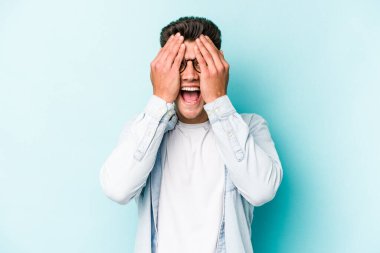 Mavi arka planda izole edilmiş genç beyaz adam yüzünün yarısını palmiye ile kaplayarak eğleniyor..