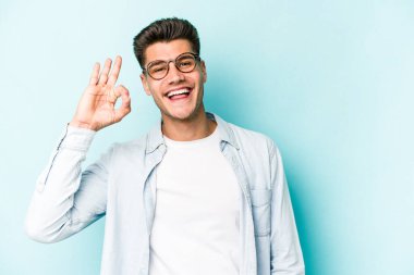 Kafkasyalı genç adam mavi arka planda izole edilmiş neşeli ve kendinden emin..