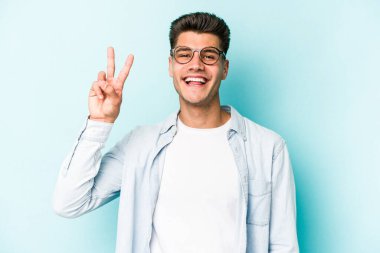 Mavi arka planda izole edilmiş genç beyaz adam iki numarayı parmaklarıyla gösteriyor..