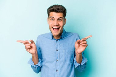 Mavi arka planda izole edilmiş genç beyaz adam farklı kopya alanlarını gösteriyor, birini seçiyor, parmaklarıyla gösteriyor.