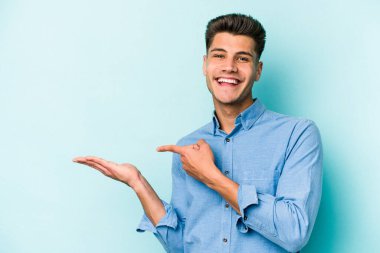 Kafkasyalı genç adam mavi arka planda izole edilmiş. Elinde palmiye ağacının bir kopyası olduğu için heyecanlı..