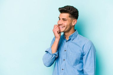 Mavi arka planda izole edilmiş genç beyaz adam rahatlamış bir şeyin fotokopi odasına baktığını düşünüyor..