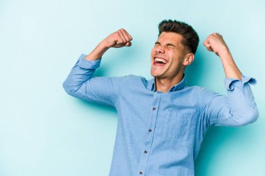 Mavi arka planda izole edilmiş genç beyaz bir adam zaferden sonra yumruğunu kaldırıyor, kazanan konsept..