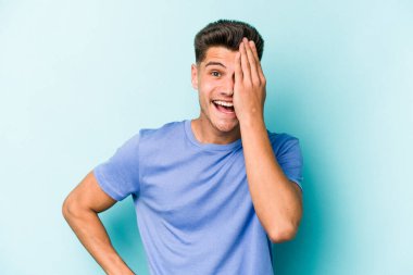 Mavi arka planda izole edilmiş genç beyaz adam yüzünün yarısını palmiye ile kaplayarak eğleniyor..