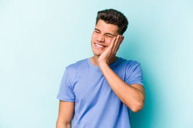 Mavi arka planda izole edilmiş genç beyaz adam kulaklarını elleriyle kapatıyor..