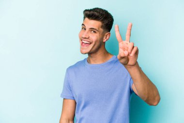 Mavi arka planda izole edilmiş genç beyaz adam iki numarayı parmaklarıyla gösteriyor..
