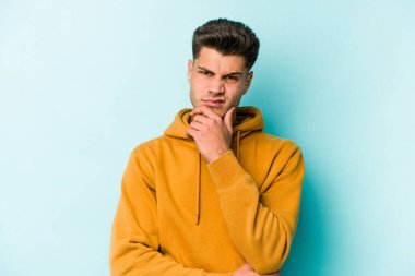 Kafkasyalı genç adam mavi arka planda izole edilmiş düşünüyor ve bakıyor, yansıtıyor, düşünüyor, bir fantezi kuruyor..