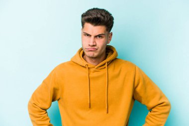Kafkasyalı genç adam mavi arka planda izole edilmiş üzgün, ciddi yüzlü, mutsuz ve hoşnutsuz..