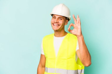 Kafkasyalı genç işçi mavi arka planda izole edilmiş neşeli ve kendinden emin..