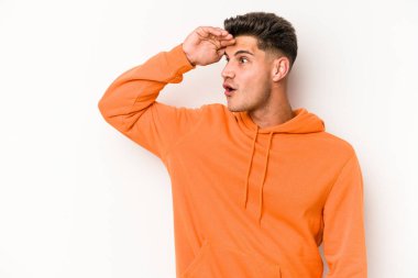 Beyaz arka planda izole edilmiş genç beyaz bir adam uzaklara bakıyor ve elini alnına koyuyor..