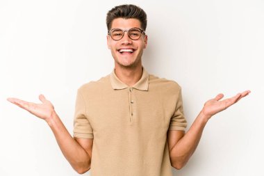 Beyaz arka planda izole genç beyaz adam kollarıyla ölçek yapar, mutlu ve kendinden emin hisseder..