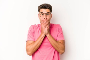 Beyaz arka planda izole edilmiş genç beyaz adam elleriyle ağzını kapatırken şok oldu..