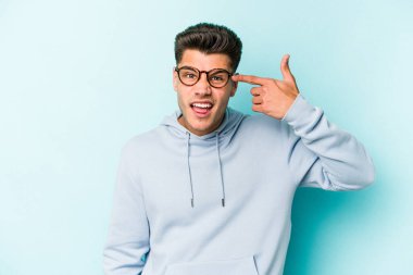 Mavi arka planda izole edilmiş genç beyaz adam işaret parmağıyla bir hayal kırıklığı jesti gösteriyor..