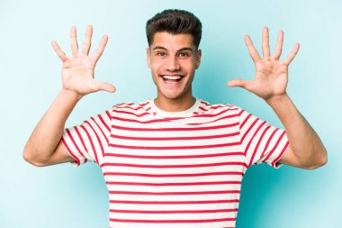 Mavi arka planda izole edilmiş genç beyaz adam on numarayı elleriyle gösteriyor..