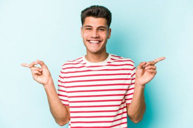 Mavi arka planda izole edilmiş genç beyaz adam farklı kopya alanlarını gösteriyor, birini seçiyor, parmaklarıyla gösteriyor.