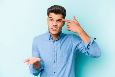 Kafkasyalı genç adam mavi arka planda izole edilmiş ve elinde bir ürün tutuyor..