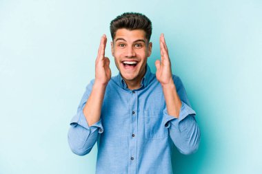 Mavi arka planda izole olmuş genç beyaz adam yüksek sesle gülüyor ve elini göğsüne koyuyor..