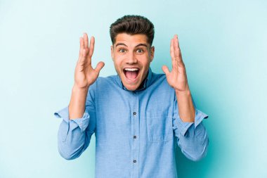 Mavi arka planda izole edilmiş genç beyaz adam hoş bir sürpriz alıyor, heyecanlı ve el kaldırıyor..
