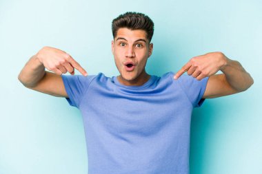 Kafkasyalı genç adam mavi arka planda izole edildi. Parmakları aşağıda, olumlu bir his var..