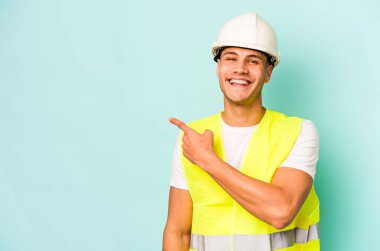 Mavi arka planda izole edilmiş genç beyaz adam gülümsüyor ve boş alanda bir şeyler gösteriyor..