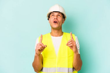 Kafkasyalı genç işçi, mavi arka planda izole edilmiş, ağzı açık, üst tarafı işaret ediyor..