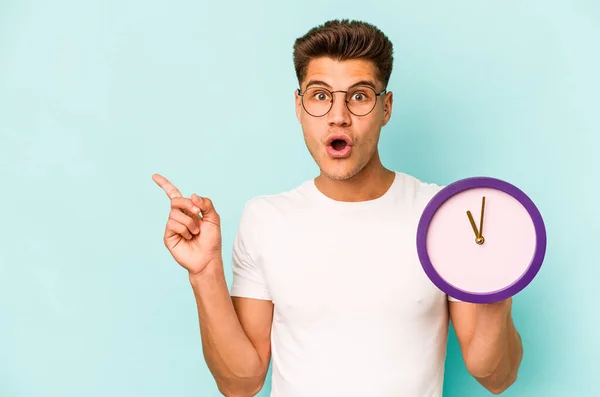Young Caucasian Man Holding Clock Isolated Blue Background Pointing Side — Φωτογραφία Αρχείου