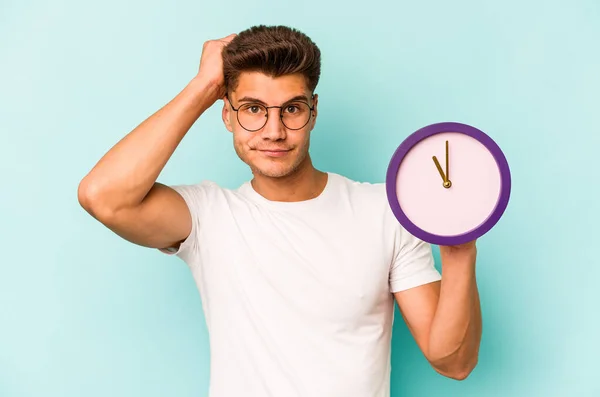 Jonge Kaukasische Man Met Een Klok Geïsoleerd Blauwe Achtergrond Wordt — Stockfoto