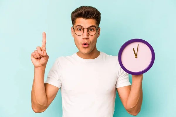 Young Caucasian Man Holding Clock Isolated Blue Background Having Some — Stockfoto