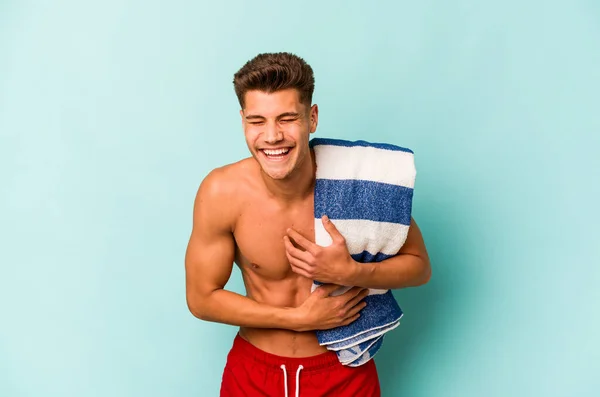 Young Caucasian Man Holding Beach Towel Isolated Blue Background Laughing — Stock fotografie
